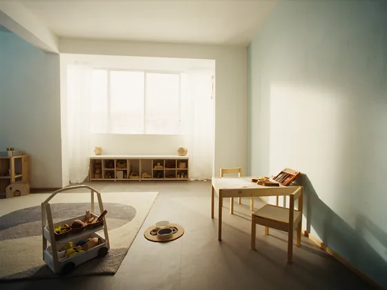 A child’s small table and chairs in a sunny playroom, with pencils, blank paper and a toy cart